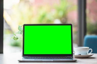 Kahve dükkanının arka planında boş ekranlı ve akıllı telefonlu dizüstü bilgisayarın bir kopyası, yeşil ekran.