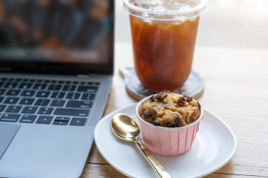 Fincan bardakta buzlu kahve ve iş konsepti sırasında kafedeki ahşap masa masasında dizüstü bilgisayarlı ev yapımı muzlu kek.
