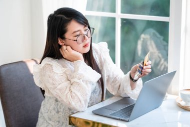 Serbest çalışan iş kadınları, internet üzerinden alışveriş yapmak ve ödeme yapmak için arka plan gibi kafelerde dizüstü bilgisayarla çalışan bir kredi kartını elinde tutarak borçlarını ağır bir şekilde düşünürler..