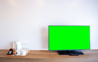 Boş yeşil ekranlı televizyon ve kahve makinesi olan monitör, alüminyum elektrikli su ısıtıcısı, temiz beyaz bardak, otel odasındaki tuğla duvardaki beyaz şeker
