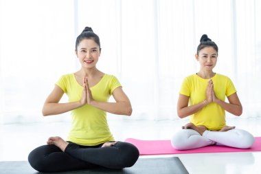 İki genç Asyalı kadın sarı elbiseyle yoga yapıyor ya da spor salonunda bir antrenörle poz veriyor ve meditasyon yapıyor sağlık yaşam tarzı ve sağlık konsepti uyguluyor..