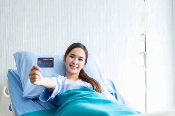 アジアの若い女性患者の笑顔の顔を示す部屋の病院の背景にベッドの上に横たわるクレジットカードを保持し 支払い医療の概念 — ストック写真