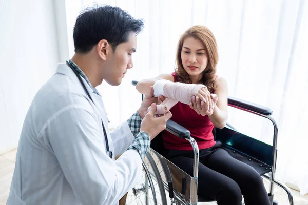 Kadın bir hastanın koluna sargı bezi saran doktor adam kol bandı takıyor. Daha iyi iyileşmek için analog basınç göstergesi takıyor..