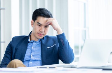 Stresli iş adamı dizüstü bilgisayarla çalışıyor ve ofis odasındaki kayıplardan sonra baş ağrısı çekiyor..