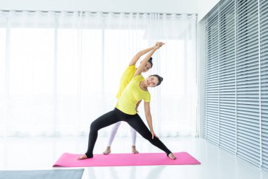 İki genç Asyalı kadın sarı elbiseyle yoga yapıyor ya da spor salonunda bir antrenörle poz veriyor ve meditasyon yapıyor sağlık yaşam tarzı ve sağlık konsepti uyguluyor..