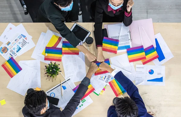 top view Successful workers Group of asian business partners wearing protective mask casual with diverse genders LGBT putting their hands together with Paper LGBT Flag at it at meeting in room office