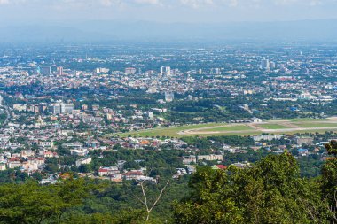 Şehir merkezinin, otelin, alışveriş merkezinin, tapınağın ve evlerin üzerindeki dağların manzarası beyaz bulutlu gökyüzü arkaplanı Chiang Mai, Tayland