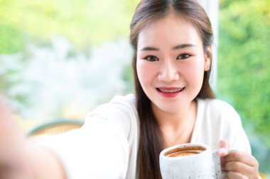 Güzel, mutlu Asyalı bir kadının portresi. Akıllı telefonuyla selfie çek. Kafenin arka planında, iş hayatı tarzı yaz tatili konseptinde rahatla.
