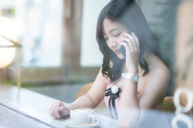 Gülümseyen Asyalı güzel bir kadının portresi rahatlıyor ve kafenin içinde oturuyor kafenin arka planında, iş hayatı tarzı yaz tatili konsepti.