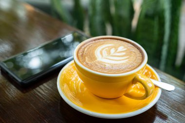 Sütlü sütlü sütlü sütlü sıcak kahve fincanı, ahşap masanın üstünde akıllı telefon. Kafedeki bir kafede kahvaltı olarak, iş konsepti sırasında, klasik tarzda.