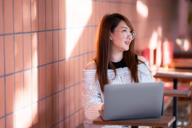 Asyalı serbest çalışan kadın iş kadını konuşuyor. İnternete göz atmak, sohbet etmek, bloglamak, akıllı telefon, kafede not defteri gibi şeyler için dizüstü bilgisayarla günlük işler yapıyor..