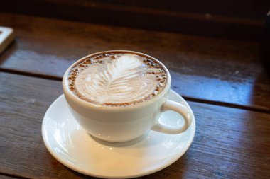 Sütlü sütlü sütlü sütlü sıcak kahve fincanı ahşap masanın üstünde. Kafedeki bir kafede kahvaltı olarak, iş konsepti sırasında, klasik tarzda.