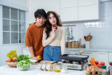 Sevgi dolu genç bir çiftin mutlu portresi. Asyalı neşeli bir şekilde yemek pişirmeyi seviyor. Sebze, et, ekmek pişiriyor.