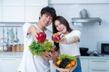 Sevgi dolu genç bir çiftin mutlu portresi. Asyalı neşeli bir şekilde yemek pişirmeyi seviyor. Sebze, et, ekmek pişiriyor.