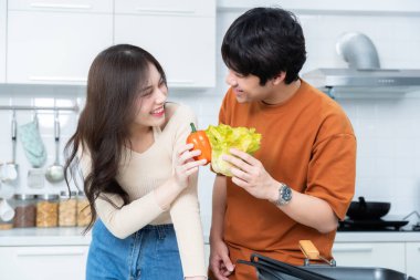 Sevgi dolu genç bir çiftin mutlu portresi. Asyalı neşeli bir şekilde yemek pişirmeyi seviyor. Sebze, et, ekmek pişiriyor.