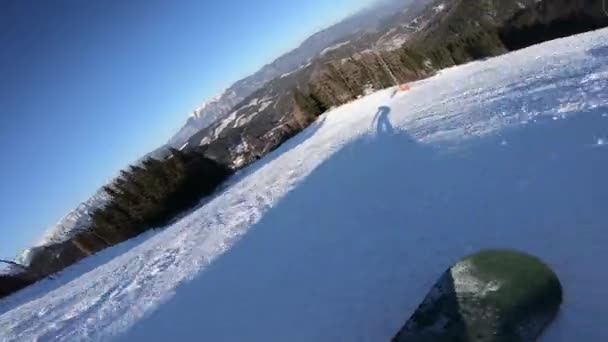 Snowboarder beweegt op een snowboard, zijn schaduw beweegt voor hem op de sneeuw synchroon — Stockvideo