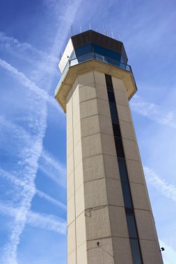 Commercial Airport Control Tower from close up perspective with sky criss-crossed by jet trails illustrating air traffic control challenges.