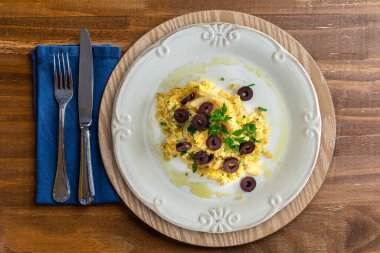 Patates kamışı, karışık yumurta ve koyu zeytinli tipik bir Portekiz morina balığı yemeği. Tahta bir masada, sarımsak, soğan, maydanoz ve diğerleriyle birlikte. Üst Manzara. Metin için boşluk.
