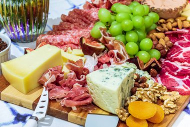 Different types of cheeses, wines, baguettes, fruits and snacks on the table for tasting and holiday scenery.