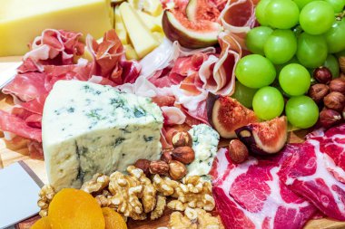 Different types of cheeses, wines, baguettes, fruits and snacks on the table for tasting and holiday scenery.
