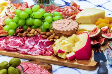Different types of cheeses, wines, baguettes, fruits and snacks on the table for tasting and holiday scenery.