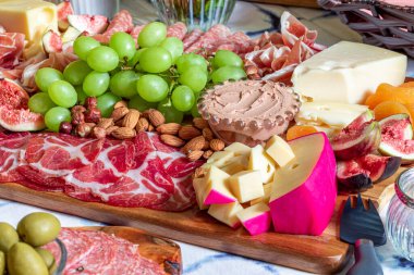 Different types of cheeses, wines, baguettes, fruits and snacks on the table for tasting and holiday scenery.