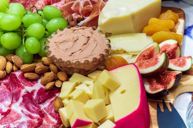 Different types of cheeses, wines, baguettes, fruits and snacks on the table for tasting and holiday scenery.