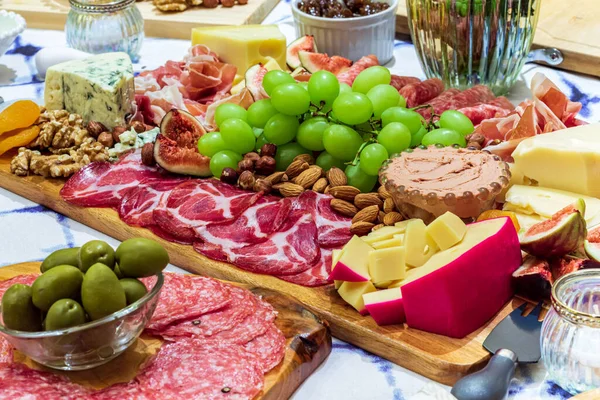 Different types of cheeses, wines, baguettes, fruits and snacks on the table for tasting and holiday scenery.