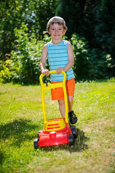 Menino feliz ajuda com jardinagem com seu cortador de grama — Fotografia de Stock