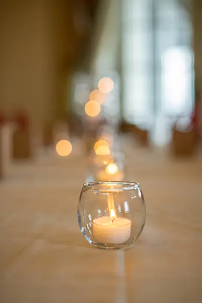 Round glass candle holder with lit candle on luxury dinner table setting