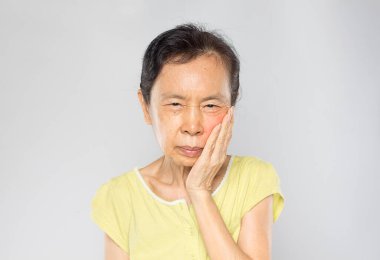old asian woman feels toothache in gray background 