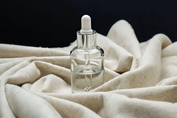 Cosmetic serum on rolled linen cloth on black background. — Stock Photo, Image