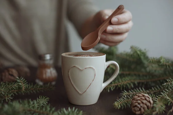 Женщина, помешивающая рождественский кофе с корицей на шоколадной ложке. Ветви ели и шишки, шоколадная ложка. — стоковое фото