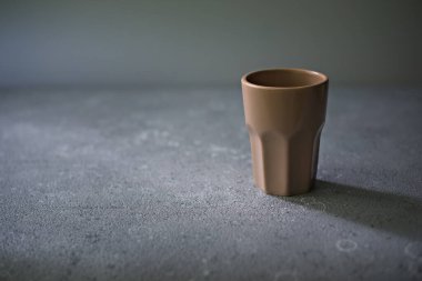 Masanın üzerinde boş bir seramik bardak duruyor. Sert ışık.