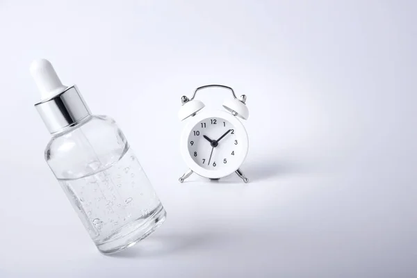 Flaska ansikte serum leviterar på en vit bakgrund bredvid retro väckarklocka. — Stockfoto