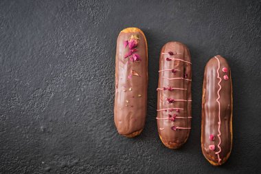 Kurutulmuş gül ve sublimleşmiş böğürtlenlerle süslenmiş çikolata kremalı ekler. Geleneksel Fransız tatlısı. Karanlık bir masada tatil için şekerler..