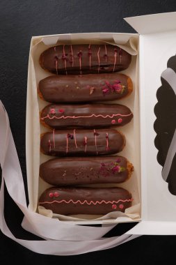 Hediye kutusunda kekler. Kurutulmuş gül ve sublimleşmiş böğürtlenlerle süslenmiş çikolata kremalı ekler. Geleneksel Fransız tatlısı. Karanlık bir masada tatil için şekerler..