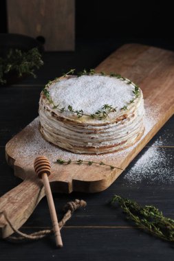 Kremalı kremalı krep, krema şekeri ve kekik filizi ile süslenmiş. Büyük bir tahtanın üzerinde tatlı. Eski bir kırsal mutfak masasında tabak.