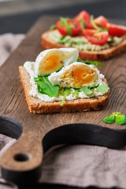 Guacamole, domates, roka ve yumurtalı tam tahıllı sandviç. Tahtada kahvaltı..