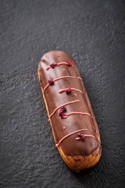 Çikolata kremalı ekler, süblimleşmiş böğürtlenlerle süslenmiş. Geleneksel Fransız tatlısı. Karanlık bir masada tatil için şekerler..