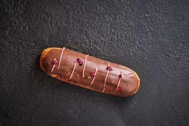 Çikolata kremalı ekler, süblimleşmiş böğürtlenlerle süslenmiş. Geleneksel Fransız tatlısı. Karanlık bir masada tatil için şekerler..