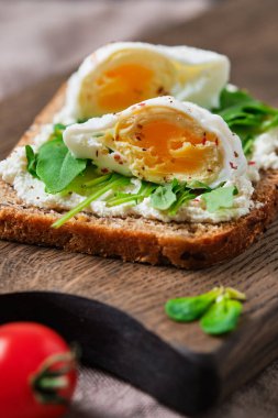 Guacamole, domates, roka ve yumurtalı tam tahıllı sandviç. Tahtada kahvaltı..