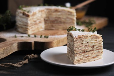 Tabakta bir dilim pasta. Kremalı kremalı krep, krema şekeri ve kekik filizi ile süslenmiş. Büyük bir tahtanın üzerinde tatlı. Eski bir kırsal mutfak masasında tabak.