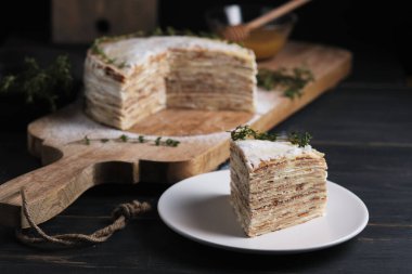 Tabakta bir dilim pasta. Kremalı kremalı krep, krema şekeri ve kekik filizi ile süslenmiş. Büyük bir tahtanın üzerinde tatlı. Eski bir kırsal mutfak masasında tabak.
