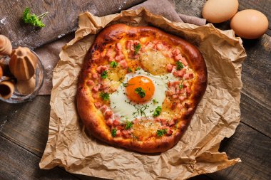 Jambonlu, peynirli, yumurtalı, domates soslu ve şifalı hamur hamurlu Rustik pizza. Tahta bir masada iştah açıcı ve lezzetli yemekler..