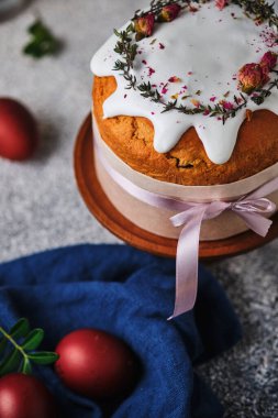 Paskalyayı kutlamak için ev yapımı kek ve kırmızı yumurta. Paskalya sembolleri. Kurumuş çiçeklerle süslenmiş Paskalya pastası, taze otlar, krema ve kurdele..