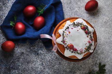 Paskalyayı kutlamak için ev yapımı kek ve kırmızı yumurta. Paskalya sembolleri. Kurumuş çiçeklerle süslenmiş Paskalya pastası, taze otlar, krema ve kurdele..