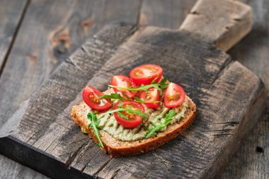Guacamole, domates ve roka ile tam tahıllı sandviç. Tahtada kahvaltı..