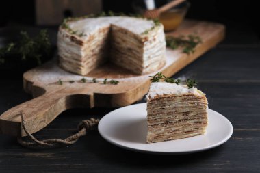 Tabakta bir dilim pasta. Kremalı kremalı krep, krema şekeri ve kekik filizi ile süslenmiş. Büyük bir tahtanın üzerinde tatlı. Eski bir kırsal mutfak masasında tabak.