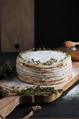 Kremalı kremalı krep, krema şekeri ve kekik filizi ile süslenmiş. Büyük bir tahtanın üzerinde tatlı. Eski bir kırsal mutfak masasında tabak.